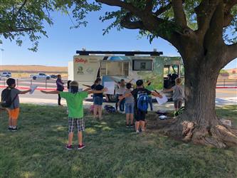 Kids learning about nutrition and fitness by doing arm circles outside in front of the Mobile Teaching Kitchen.